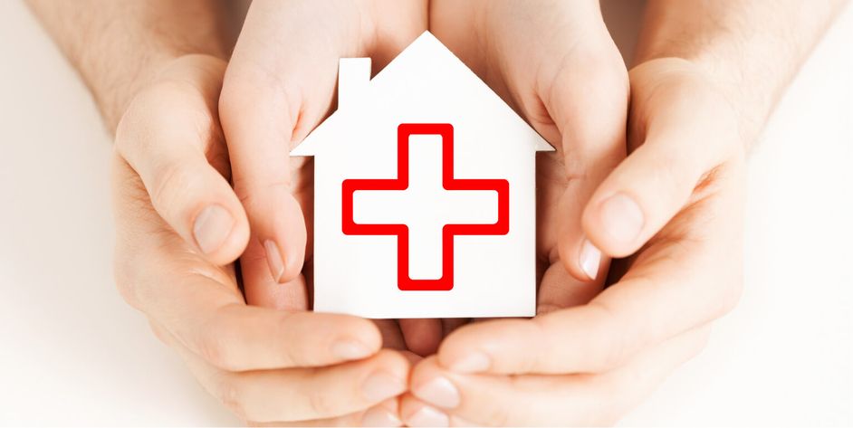 Ein Hausmodell mit großem roten Kreuz wird von zwei Personen in den Händen gehalten